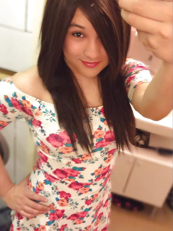 Portrait en selfie d'une jeune femme aux cheveux bruns portant une robe fleurie, souriante, devant un miroir.