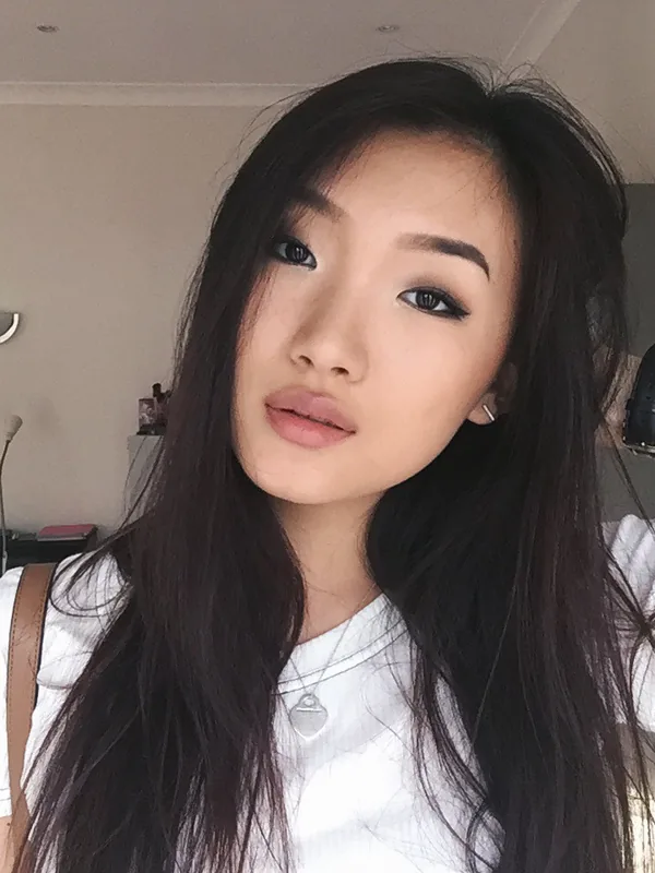 Portrait d'une jeune femme aux cheveux noirs portant un t-shirt blanc, regardant l'objectif dans un intérieur lumineux.