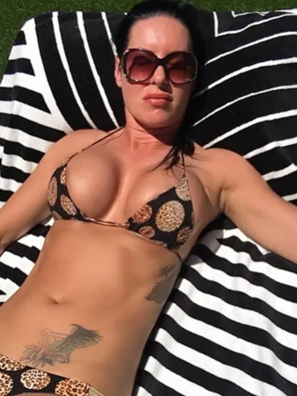 Femme allongée sur une serviette rayée, portant un maillot de bain léopard et des lunettes de soleil, sous un soleil vif.
