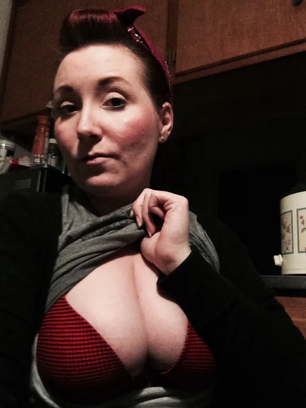 Femme aux cheveux roux en chignon, portant un bandeau rouge, un haut noir et un soutien-gorge rouge, dans une cuisine.