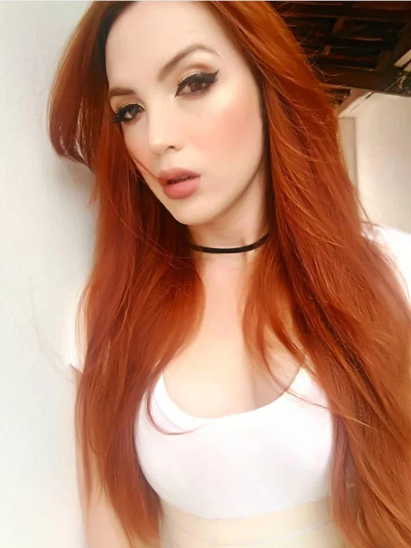 Portrait d'une femme aux cheveux roux portant un haut blanc et un collier choker, regardant l'objectif.