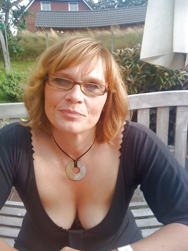 Portrait d'une femme aux cheveux blonds portant des lunettes et un haut noir, assise en extérieur.